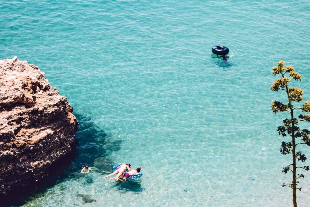 Man and Woman Swimming in the Sea Near Brown Cliff