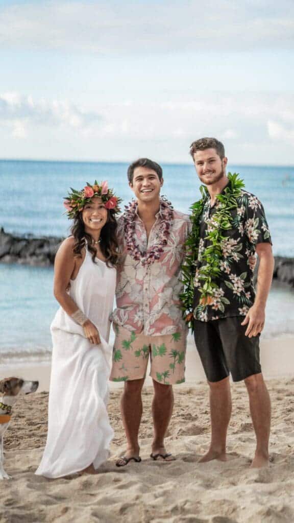 Happy newlywed diverse couple and friend standing on beach and