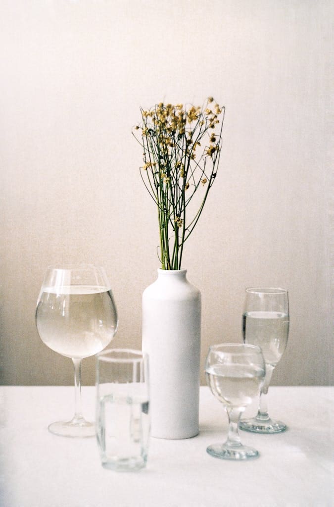 A Flowers on a Ceramic Vase Surrounded with Glass Items with Water