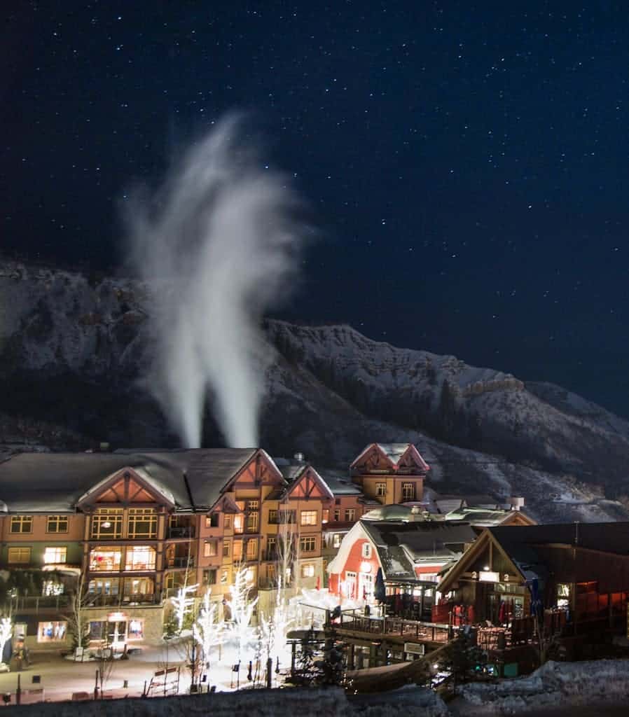 High Angle Shot Of A Beautiful Town With Wooden Buildings And Bright Lights On The Streets Surrounded By Scenic Winter Landscape