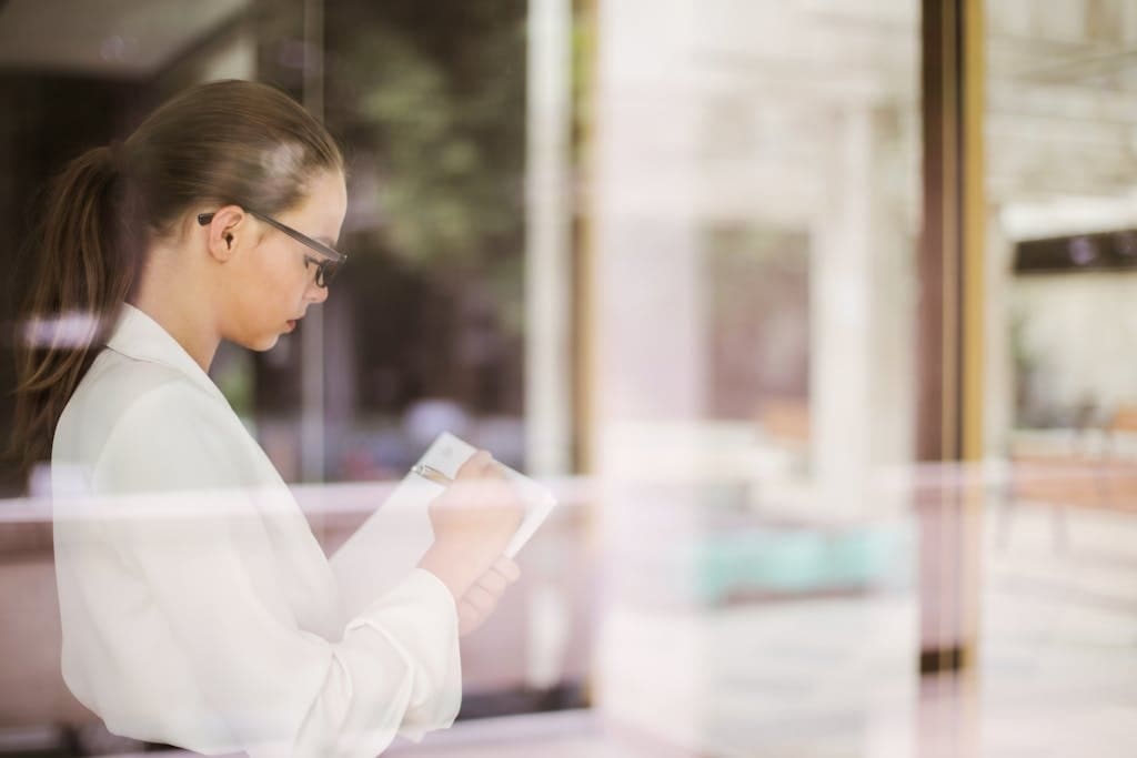 Side view of young concentrated businesswoman in formal clothing standing in office and writing ideas about startup project