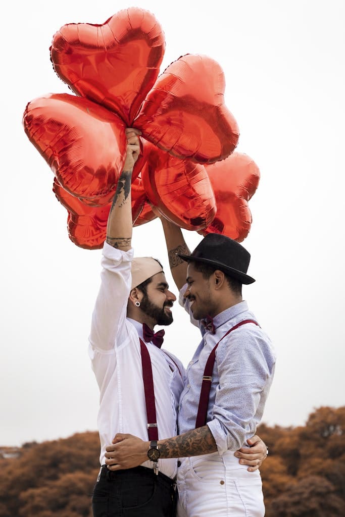 Two Men Embracing while Holding Heart Balloons