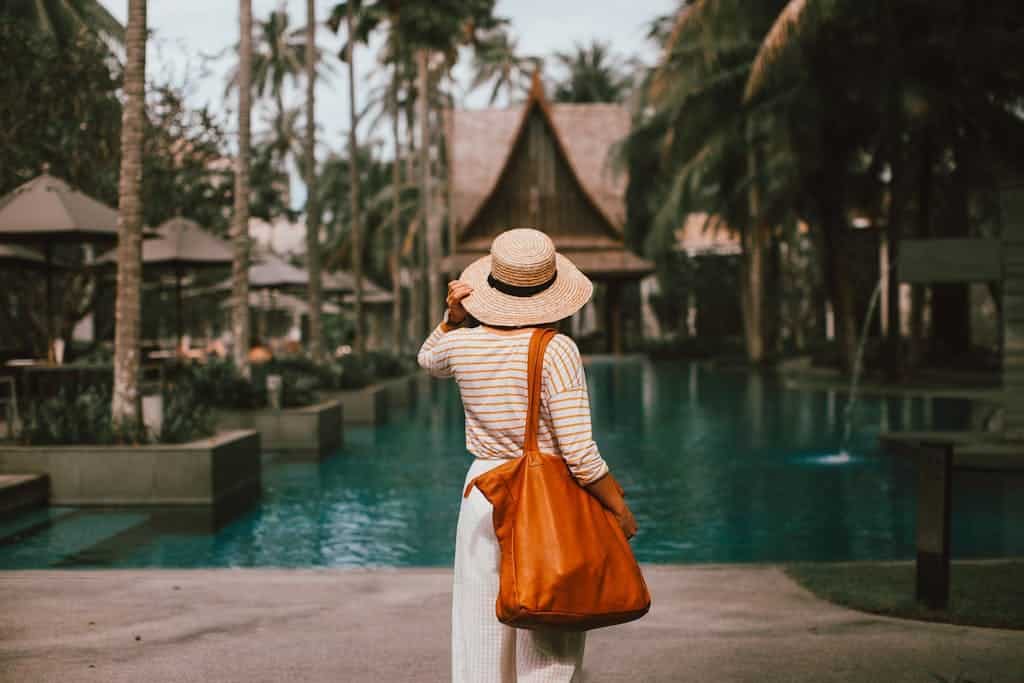 Unrecognizable woman in hat standing on poolside in resort