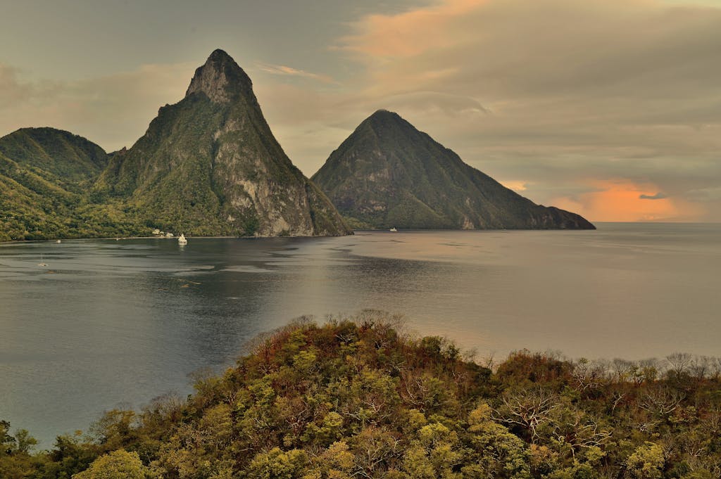 A breathtaking sunset view of the Pitons in St. Lucia with lush greenery and calm sea.