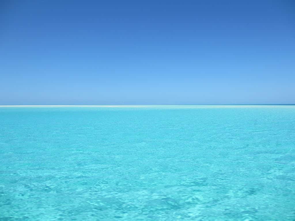 A serene blue ocean with crystal clear water under a vivid blue sky, perfect for relaxation.