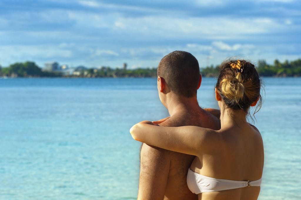 A couple embracing and enjoying the view at a sunny tropical beach, symbolizing love and relaxation.