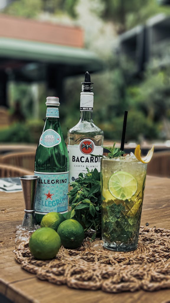 A detailed shot of a mojito cocktail featuring Bacardi rum, soda water, lime, and mint leaves on a wooden table.