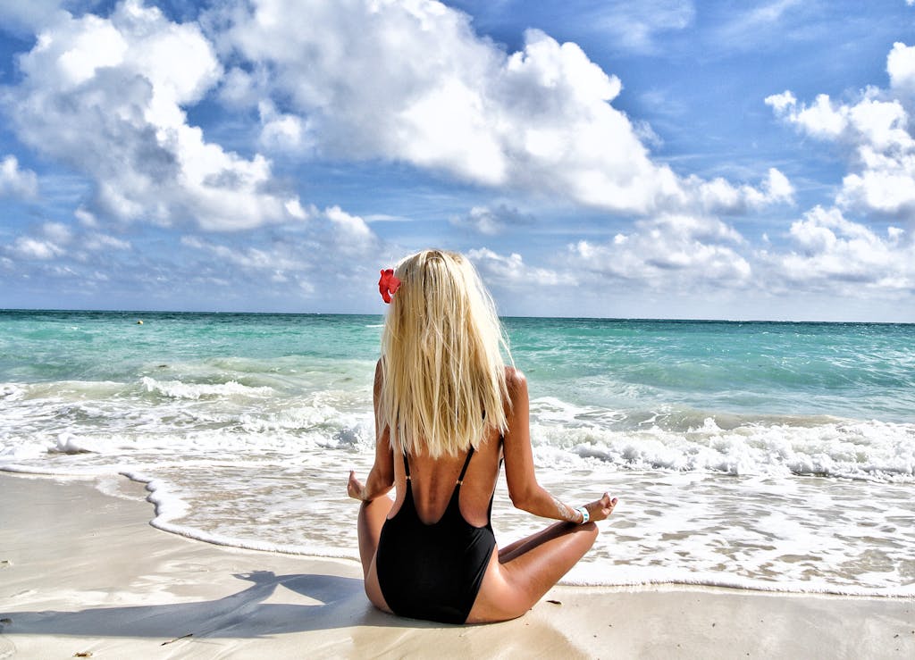 A woman meditates on a beautiful tropical beach in the Bahamas, under a clear blue sky.