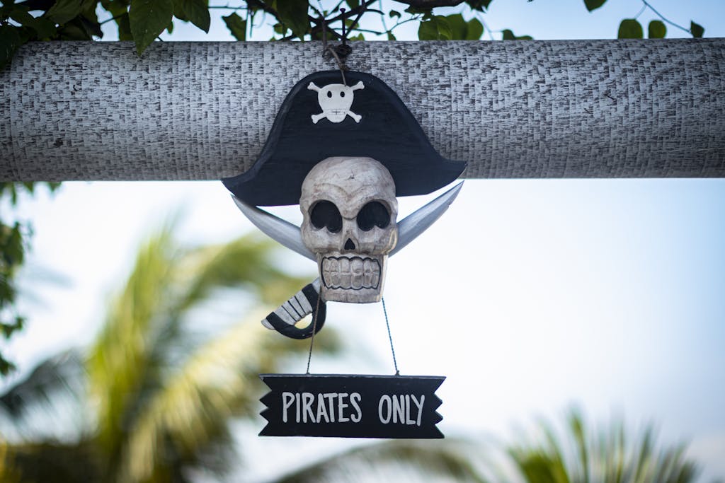 Decorative pirate skull sign with 'Pirates Only' text hanging outdoors on a sunny day.