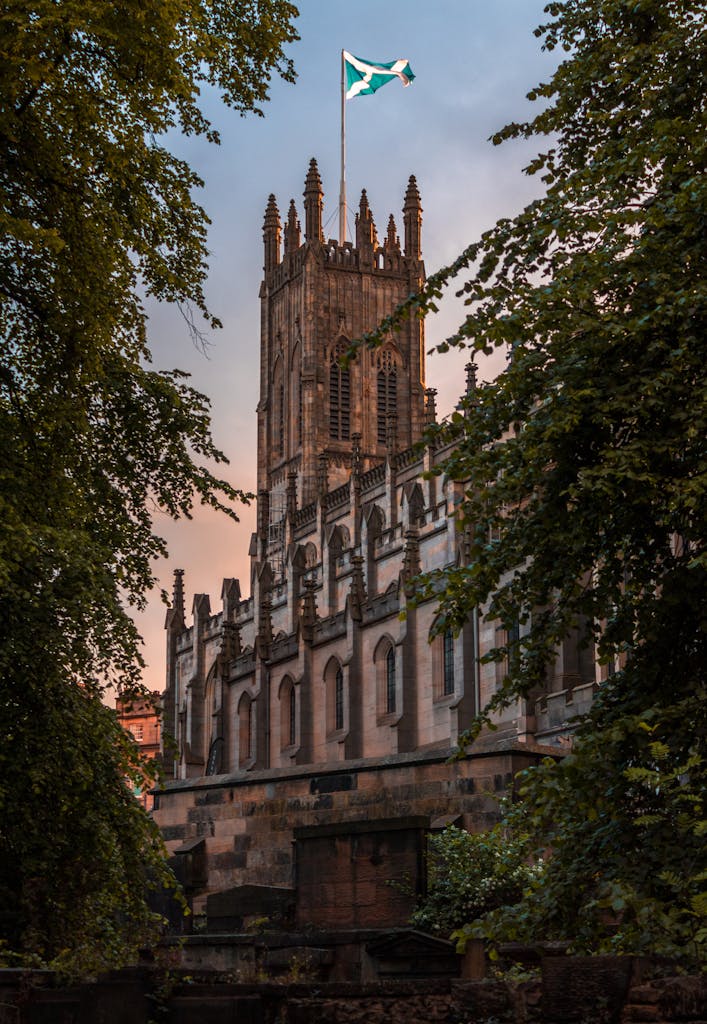 Majestic Gothic building in Edinburgh with a Scottish flag, framed by lush greenery.