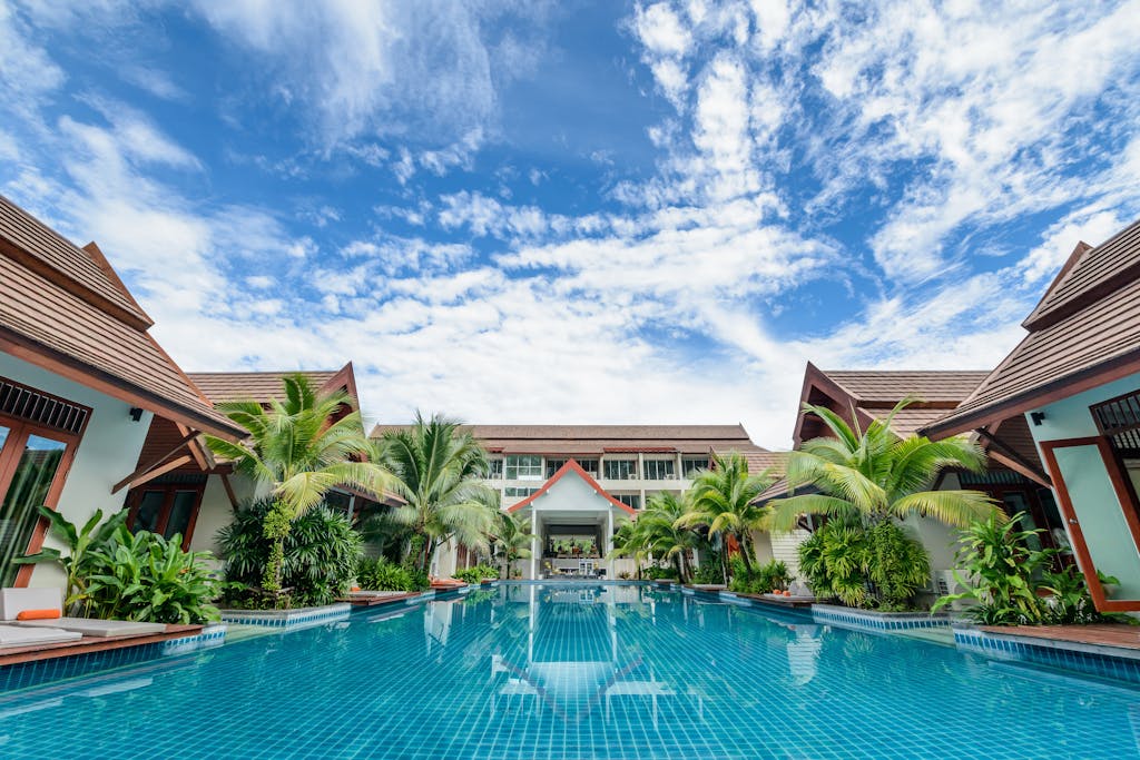 Spacious swimming pool surrounded by tropical villas under a bright blue sky, perfect for relaxation.